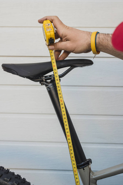 黄色いテープを使ってマウンテンバイクのシート高を測定する男。自転車の座席のサービスと設定. - 写真・画像