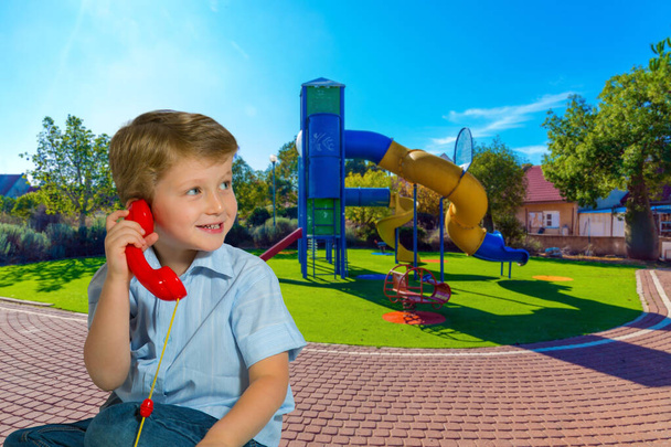  Great kids playground. Attraction "Spiral hill with a closed descent". Handsome blond boy with blue eyes speaks on a red telephone. The concept of physical and mental development of children - Фото, зображення