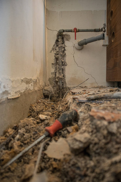 アパートの水道管が壊れた。タイル、古いコンクリートや破片で地面に見える穴。壁にパイプと閉弁で自宅の漏水を改善しようとしている間の建設現場 - 写真・画像