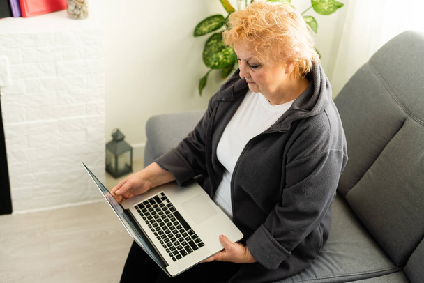 Dizüstü bilgisayara bakan yaşlı bir kadın. akrabalarla çevrimiçi video iletişimi - Fotoğraf, Görsel
