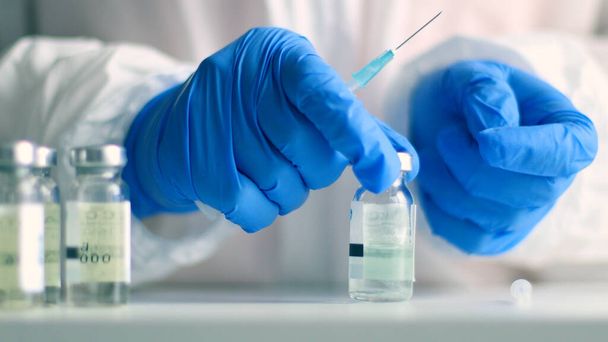 Orvos kék gumikesztyűben töltse ki a fecskendőt injekciós üvegből készült gyógyszerrel egy idős személy orvosi laboratóriumban coronavirus, influenza, kanyaró betegség ellen - Fotó, kép