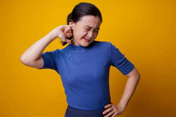 Aziatische vrouw jeuk en het plaatsen van een vinger in haar oren staan geïsoleerd over gele achtergrond. - Foto, afbeelding