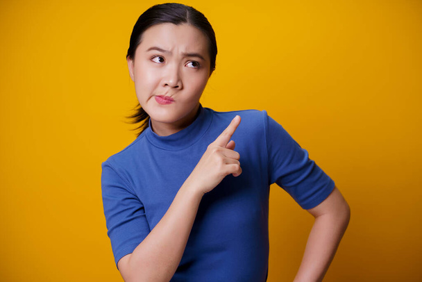 Confused Asian woman thinking and standing isolated on yellow background. - Photo, Image
