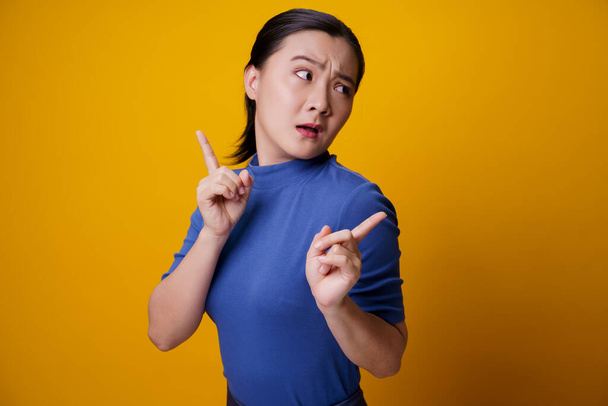 Confused Asian woman thinking and standing isolated on yellow background. - Photo, Image
