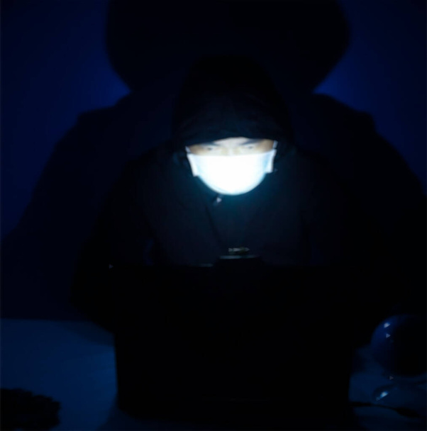 Blurry imagr Hacker en frente de su máscara facial con capucha pirata informático robando información financiera y noticias falsas con un ordenador portátil. - Foto, Imagen
