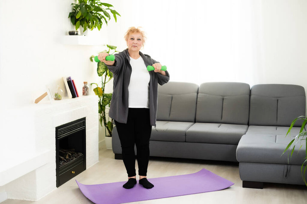 Ajuste mujer mayor feliz haciendo ejercicios de estiramiento en su esterilla de yoga - Foto, imagen