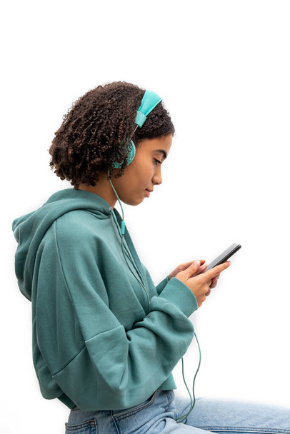 Афроамериканский подросток в бирюзовых наушниках и в толстовке с помощью смартфона и прослушивания музыки - Фото, изображение