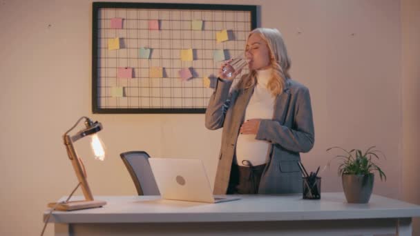Empresaria embarazada bebiendo agua y tocando el vientre en la oficina - Imágenes, Vídeo