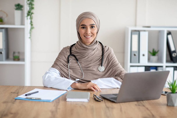Portrait of smiling female doctor sitting at workdesk in clinic - Photo, Image