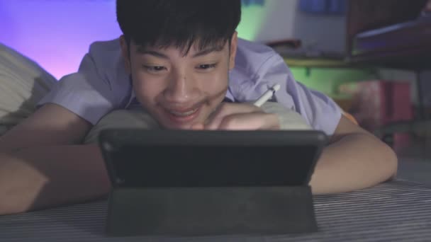 Adolescente utiliza una tableta para jugar juegos en línea en una habitación decorada con iluminación RGB. - Metraje, vídeo