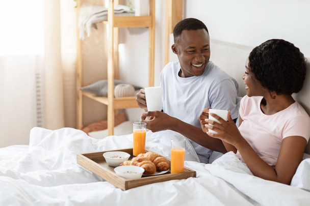 Радостная черная пара завтракает в постели дома - Фото, изображение