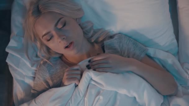 widok z góry chorej kobiety kichającej podczas leżenia w łóżku w nocy - Materiał filmowy, wideo