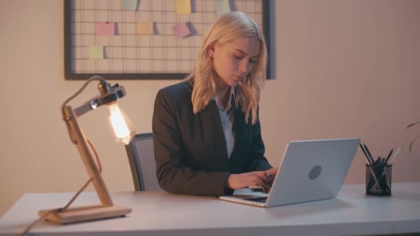 donna d'affari bionda digitando sulla tastiera del computer portatile mentre si lavora in serata - Filmati, video