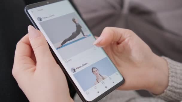 Young girl browses social media on the phone and likes the photo. The girl browses the new posts of a fitness trainer in the social network application and begins to follow. Mobile phone close up - Footage, Video