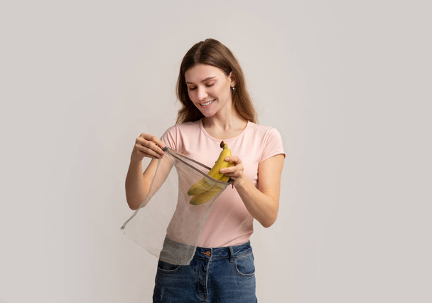 Zero Waste Shopping. Glückliche Millennial-Frau steckt Bananen in Mehrwegtasche - Foto, Bild