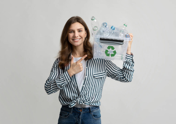 Alegre eco voluntario mujer señalando el envase con residuos de plástico para el reciclaje - Foto, Imagen