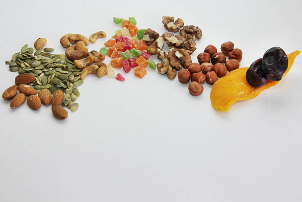 Proper nutrition without sweets. Replacing sweets with nuts and dried fruits, mangoes, dates, green pumpkin seeds, almonds, hazelnuts, walnuts, on a white background - Foto, Imagen