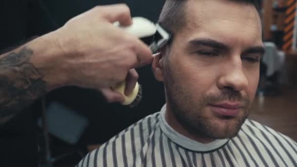 Tatuado barbeiro aparar o cabelo do homem na barbearia - Filmagem, Vídeo
