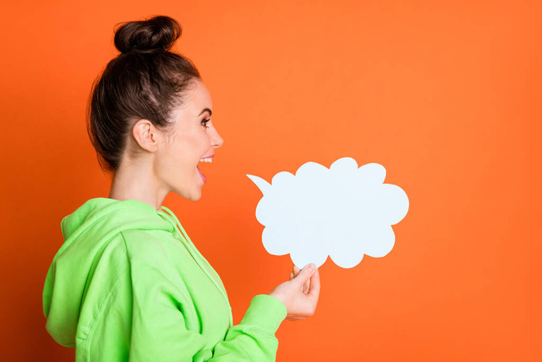 Photo of charming young lady dressed green sweatshirt talking looking paper cloud isolated bright orange color background - Photo, Image