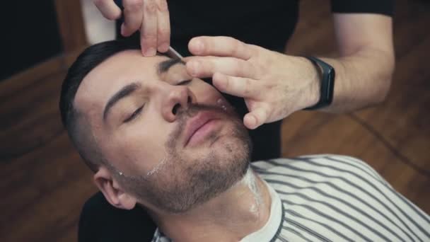 Peluquero afeitado hombre en capa en la barbería  - Metraje, vídeo