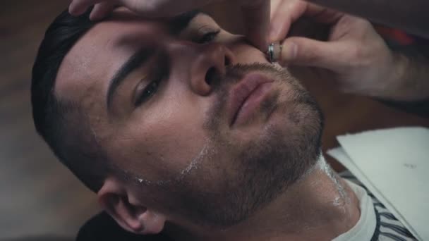 Peluquero usando maquinilla de afeitar mientras trabaja con el cliente  - Imágenes, Vídeo