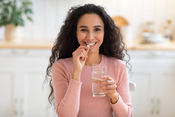 Beauty Supplement. Smiling Brunette Woman Taking Vitamin Pill And Drinking Water - 写真・画像