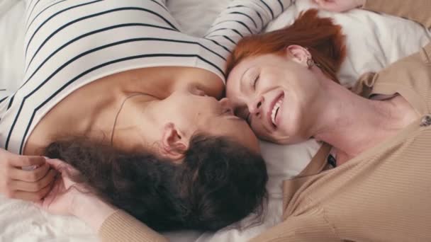 προβολή υψηλής γωνίας του ευχαριστημένου διαφυλετικού λεσβιακού ζευγαριού ξαπλωμένο στο κρεβάτι - Πλάνα, βίντεο