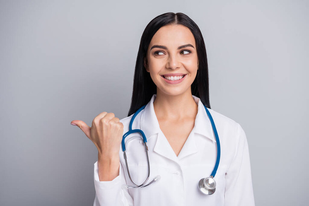 Photo of doctor girl direct thumb look empty space wear stethoscope white uniform isolated grey color background - Valokuva, kuva