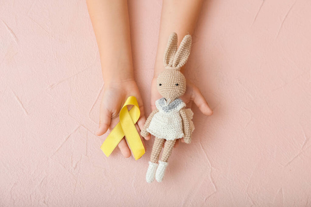 Hands with toy and golden ribbon on color background. Childhood cancer awareness concept - Photo, Image