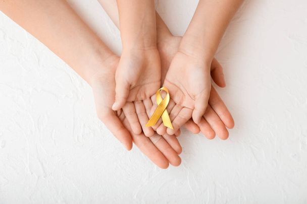 Hands with golden ribbon on white background. Childhood cancer awareness concept - Foto, imagen