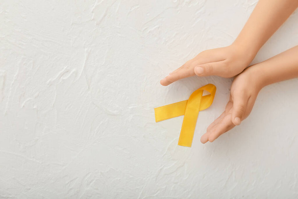 Beyaz arka planda altın kurdeleli eller. Çocukluk kanseri farkındalığı - Fotoğraf, Görsel