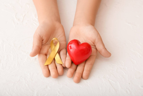 Mani con cuore rosso e nastro dorato su sfondo bianco. Concetto di consapevolezza del cancro infantile - Foto, immagini