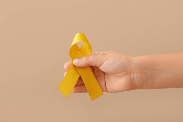 Hand with golden ribbon on color background. Childhood cancer awareness concept - Foto, imagen