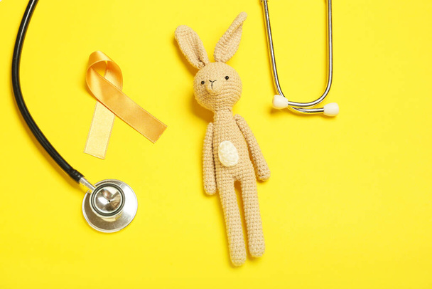 Golden ribbon, stethoscope and toy on color background. Childhood cancer awareness concept - Foto, afbeelding