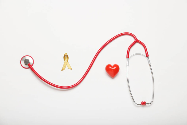 Золотая лента, стетоскоп и сердце на белом фоне. Концепция информированности детей о раке - Фото, изображение