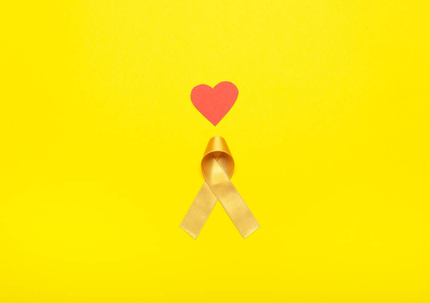 Golden ribbon and red heart on color background. Childhood cancer awareness concept - Photo, Image