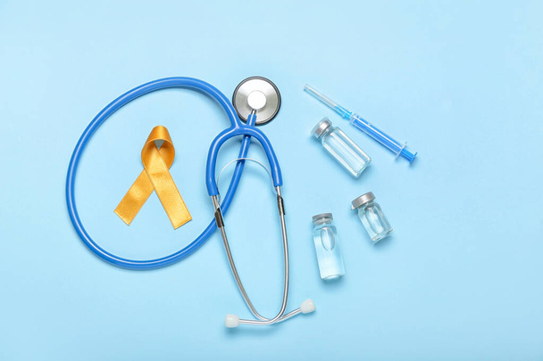 Nastro dorato, stetoscopio e rimedio su sfondo a colori. Concetto di consapevolezza del cancro infantile - Foto, immagini