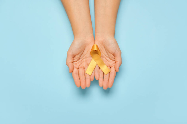 Hands with golden ribbon on color background. Childhood cancer awareness concept - Foto, imagen