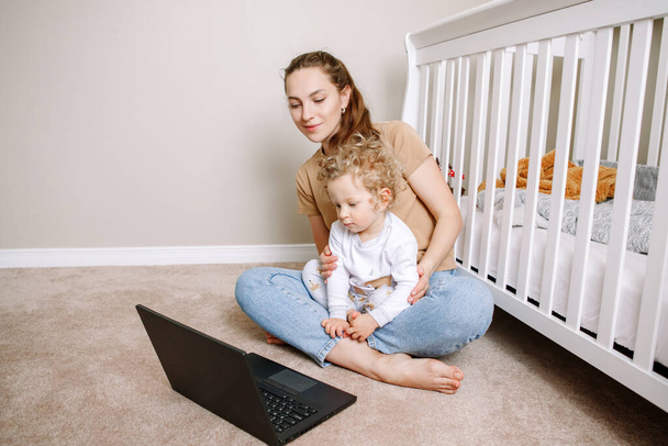 Young Caucasian mother with toddler baby boy watching cartoons on laptop at home. Family mom with kid using technology. Video chat, video call. Screen time for kids. - Photo, Image