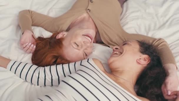 Blick aus der Vogelperspektive auf zufriedene interrassische lesbische Paare, die lachen und auf dem Bett liegen - Filmmaterial, Video