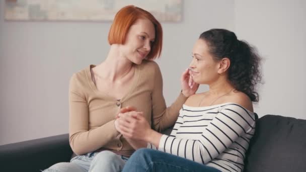 interracial lesbian couple holding hands and smiling in living room - Filmagem, Vídeo