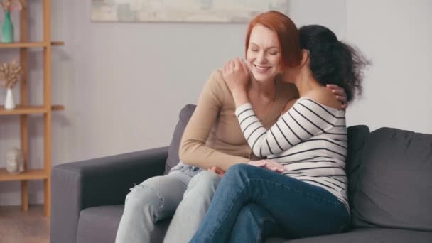 διαφυλετικό λεσβιακό ζευγάρι αγκαλιάζει και χαμογελά στο σαλόνι - Πλάνα, βίντεο