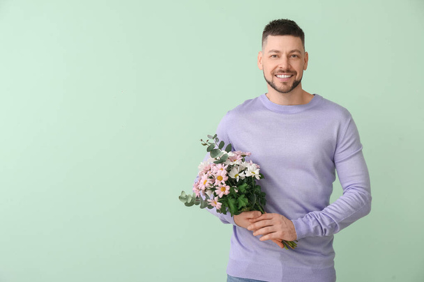 Schöner Mann mit einem Strauß schöner Blumen auf farbigem Hintergrund - Foto, Bild