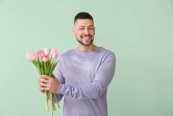 Schöner Mann mit einem Strauß schöner Blumen auf farbigem Hintergrund - Foto, Bild