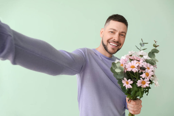 Handsome man with bouquet of beautiful flowers taking selfie on color background - Foto, imagen
