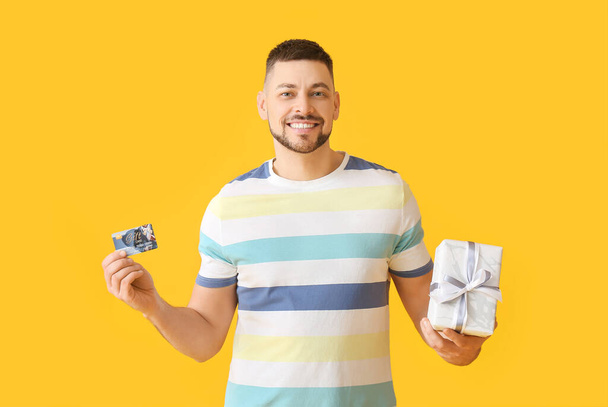 Schöner Mann mit Geschenkkarte und Geschenk auf farbigem Hintergrund - Foto, Bild