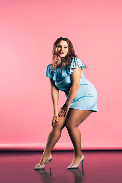 Happy sexy plus size model in blue dress on pink background, body positive concept - Foto, imagen