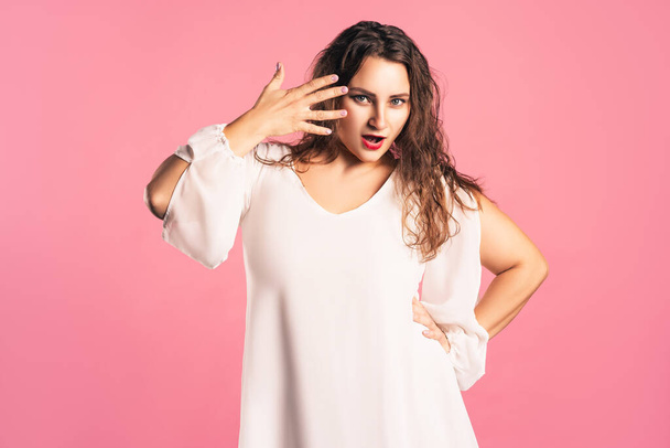 Amazed plus size model with wide open mouth on pink background, body positive concept - Zdjęcie, obraz
