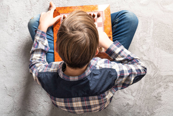 biały nastolatek chłopiec gra w szachy w szary dywan, edukacja, aktywność i hobby w domu koncepcja - Zdjęcie, obraz