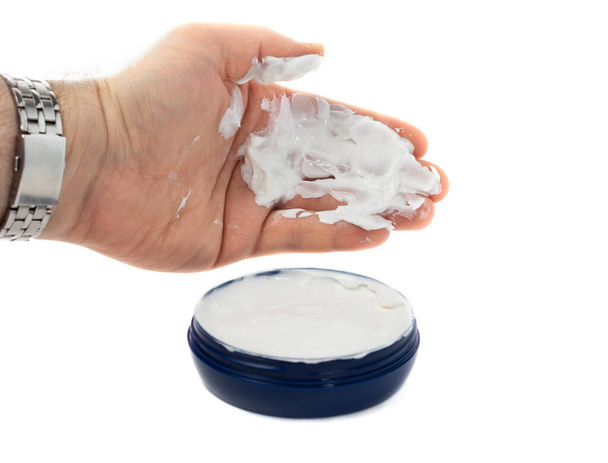 the man takes with his palm a white hand cream from a blue jar. beauty concept, dry skin, skin hydration. White background. copy space. - Photo, Image